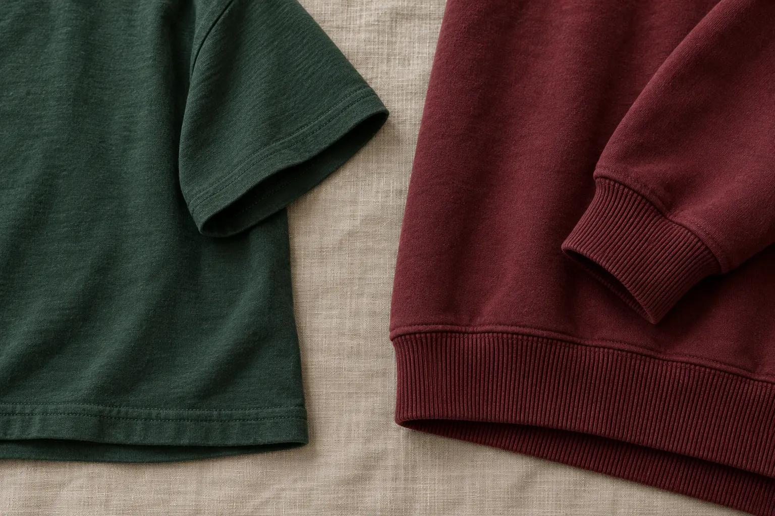 Side-by-side detail of two garments on a neutral linen surface: the open straight hem and short sleeve of a forest green