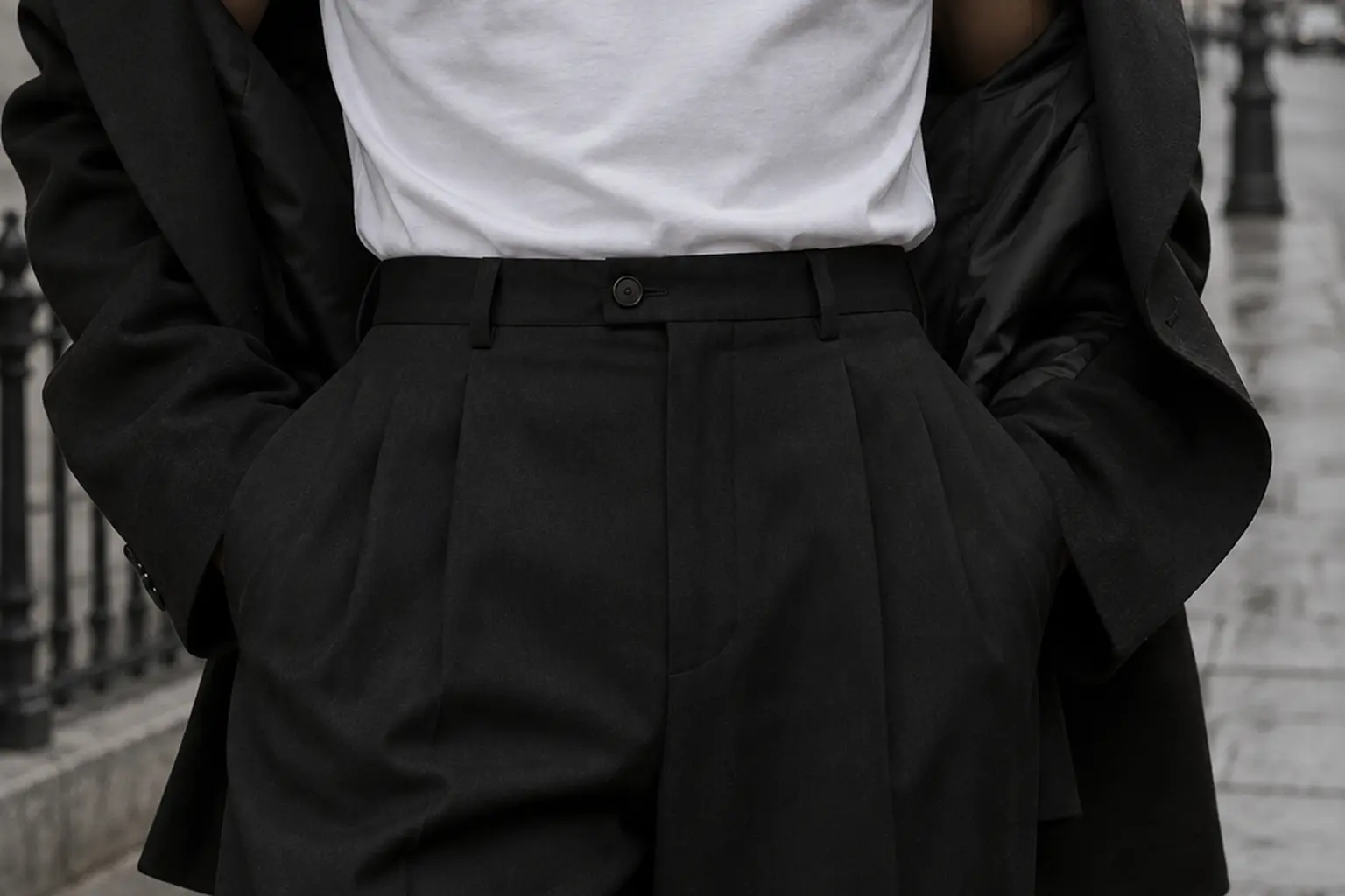 A person seen from the neck down in a plain white tee tucked fully into high-waisted black trousers, standing on a quiet